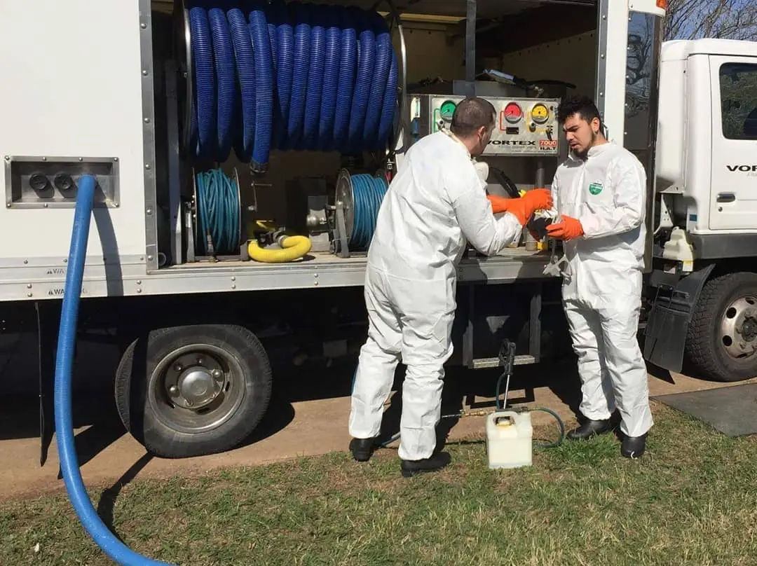 Two workers in white overalls fixing their restoration equipment in a truck.