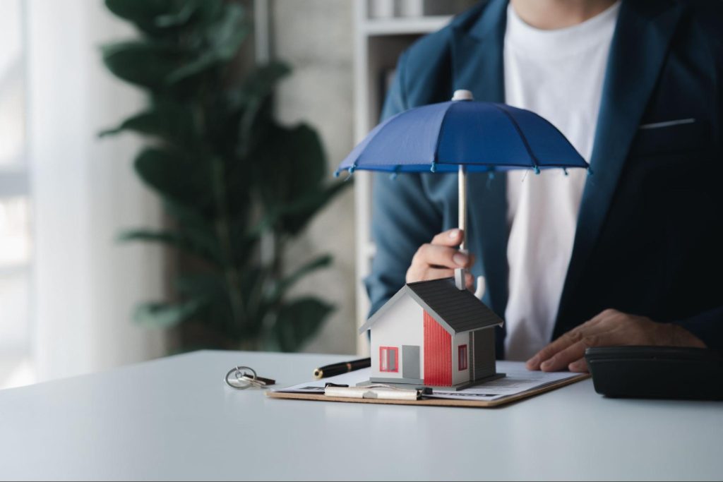 Man holding an umbrella over a home on insurance documents.