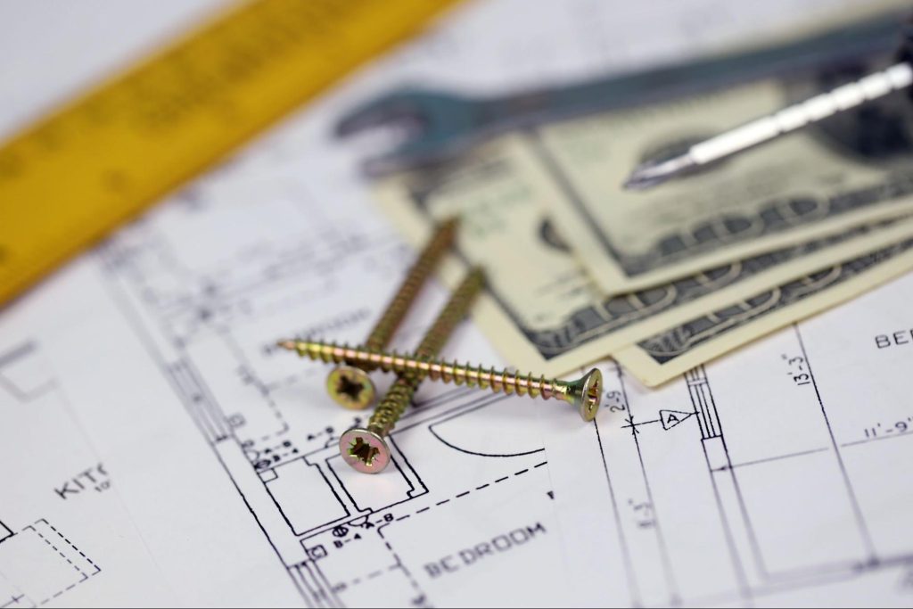Money next to nails, tools, measuring tape, and blueprints.