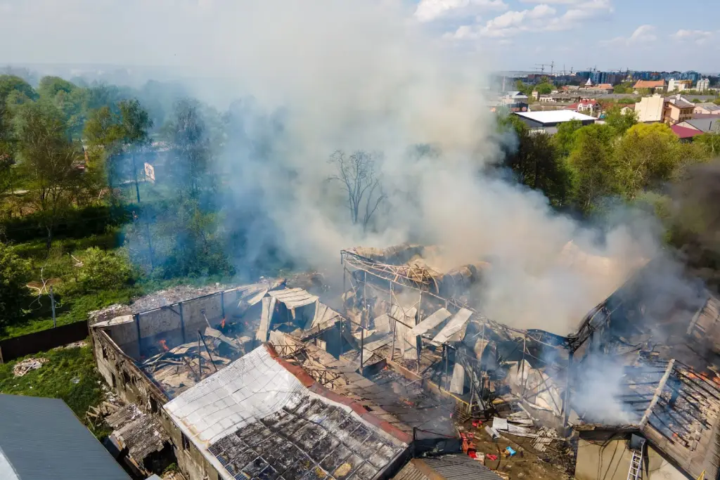 Aerial view of a fire-damaged building with a collapsed roof and thick dark smoke rising into the sky.