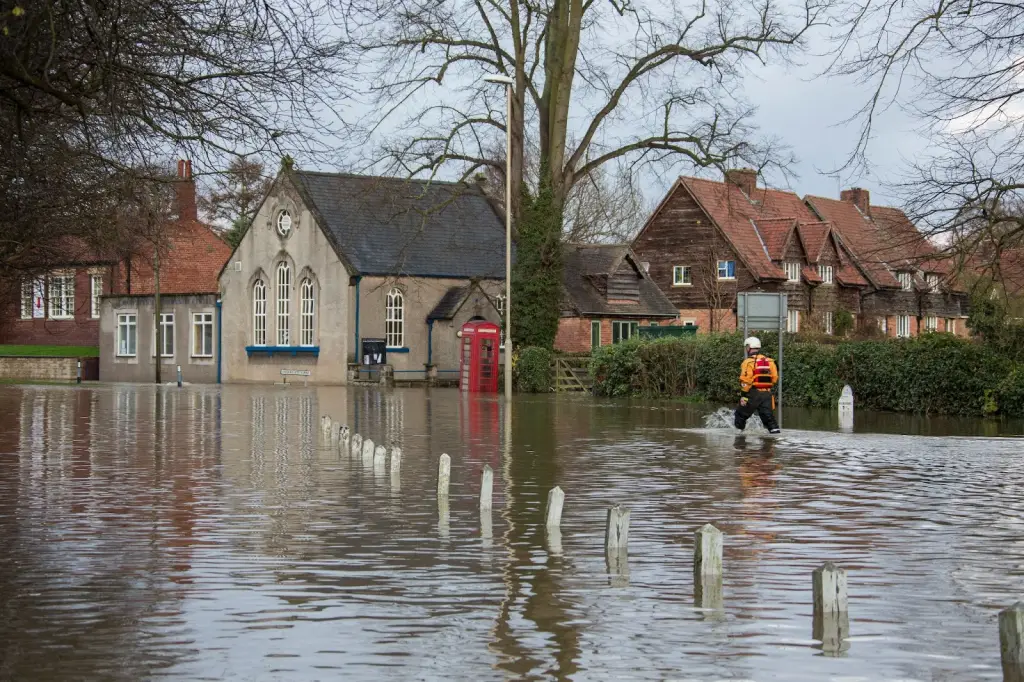 A man wades through deep floodwaters on a rural road as he returns to his village.