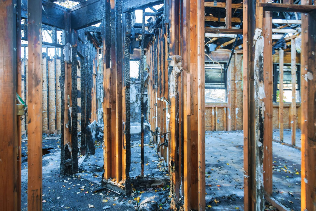 ALT TEXT: Charred remains stand where a complete building once stood.