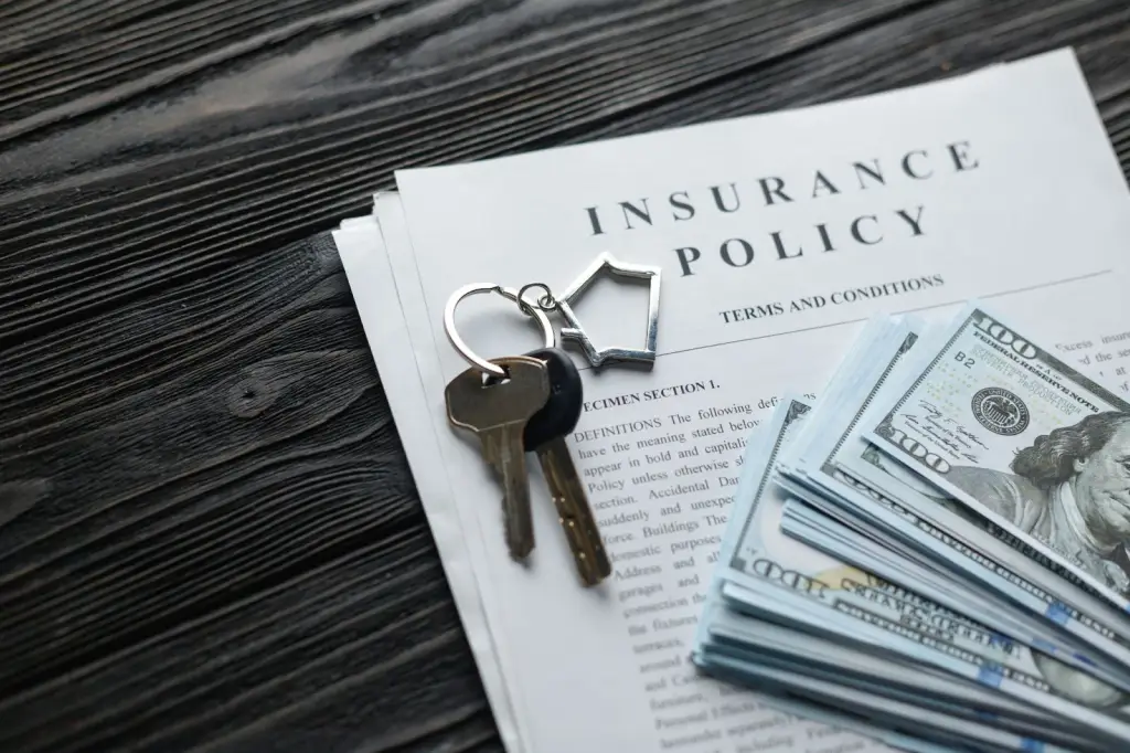 A close-up of home insurance papers with money and house keys.
