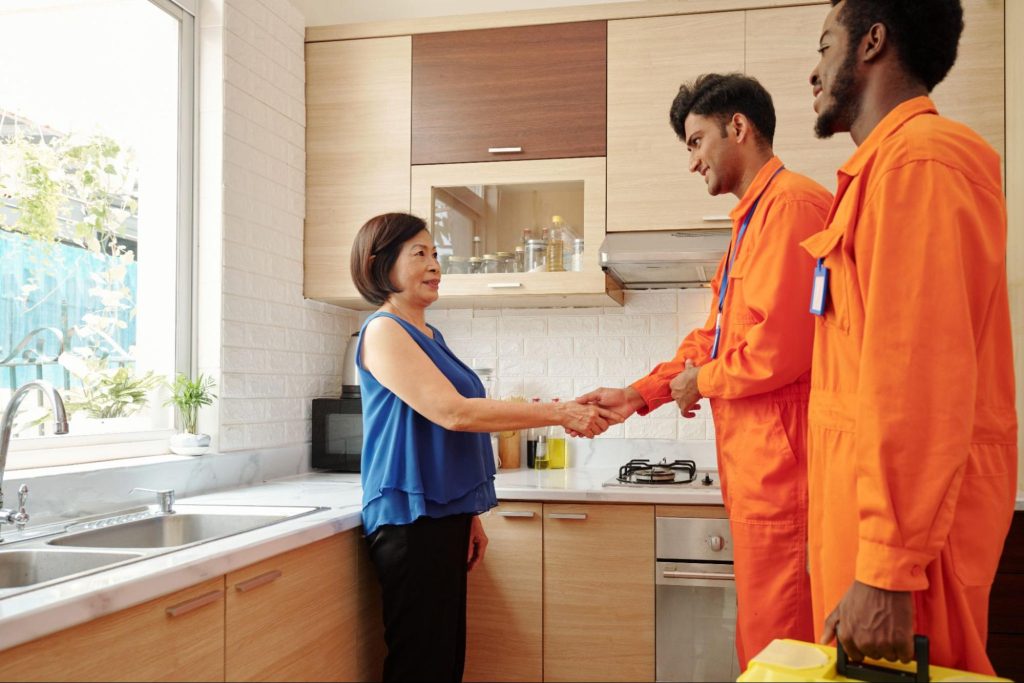Two employees of a restoration company in uniform shaking the hand of a homeowner.