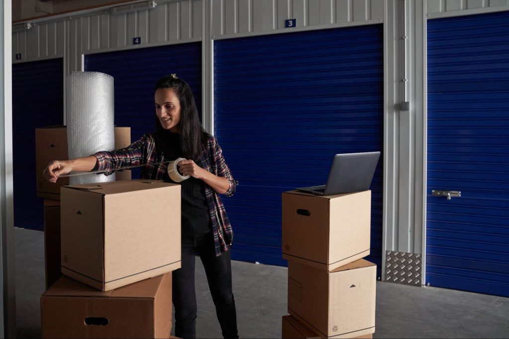 Woman packing boxes with scotch tape in front of temperature controlled storage.
