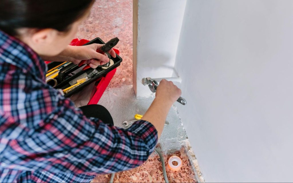 A female plumber tightens a pipe with a wrench, ensuring proper repairs for fixing water damage.