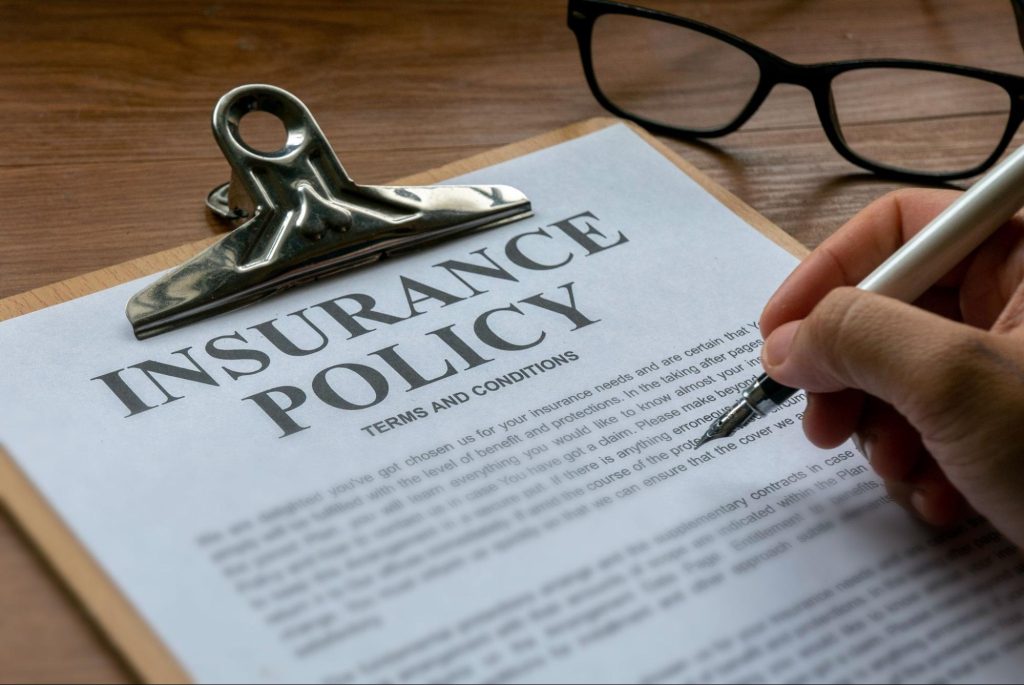 A person holding a pen while reading an insurance policy attached to a clipboard.