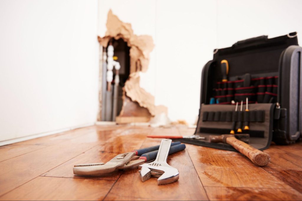 Tools and a toolbox lying on the floor next to a damaged wall.